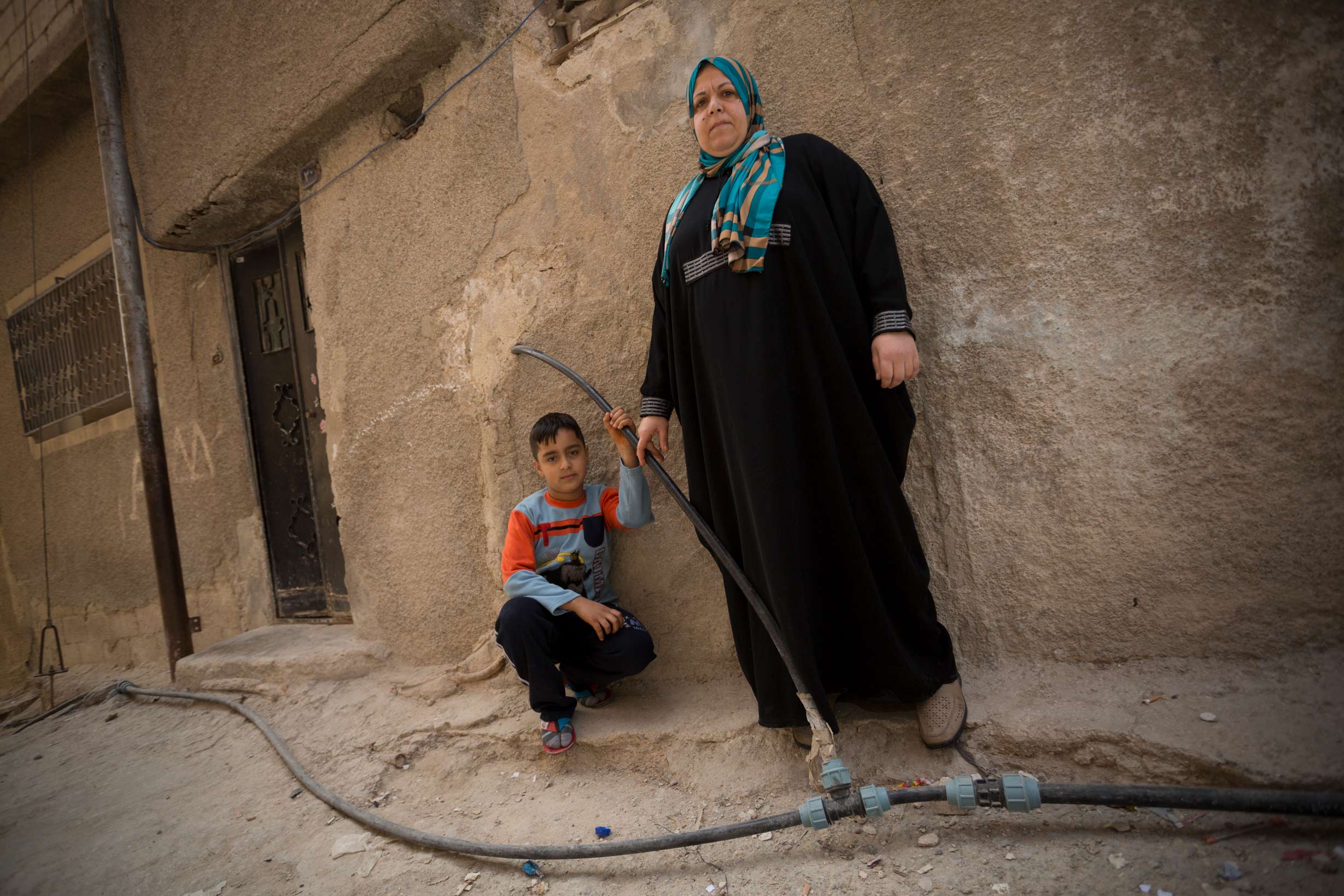 Mrs. Um Osama Omran and her son Sari stand among exposed municipal water pipes outside their home in Zarqa, Jordan in 2013. As part of a $275 million compact with Jordan, which closed in 2017, MCC has rehabilitated Zarqa's antiquated drinking and wastewater network and helped to expand a new wastewater treatment facility, all of which increased available water for drinking and irrigation and improved the safety and living conditions of the city's residents.