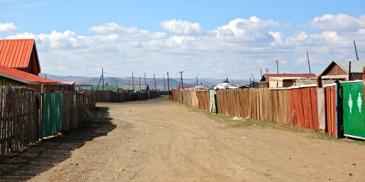 A dirt road in Mongolia with houses on either side.
