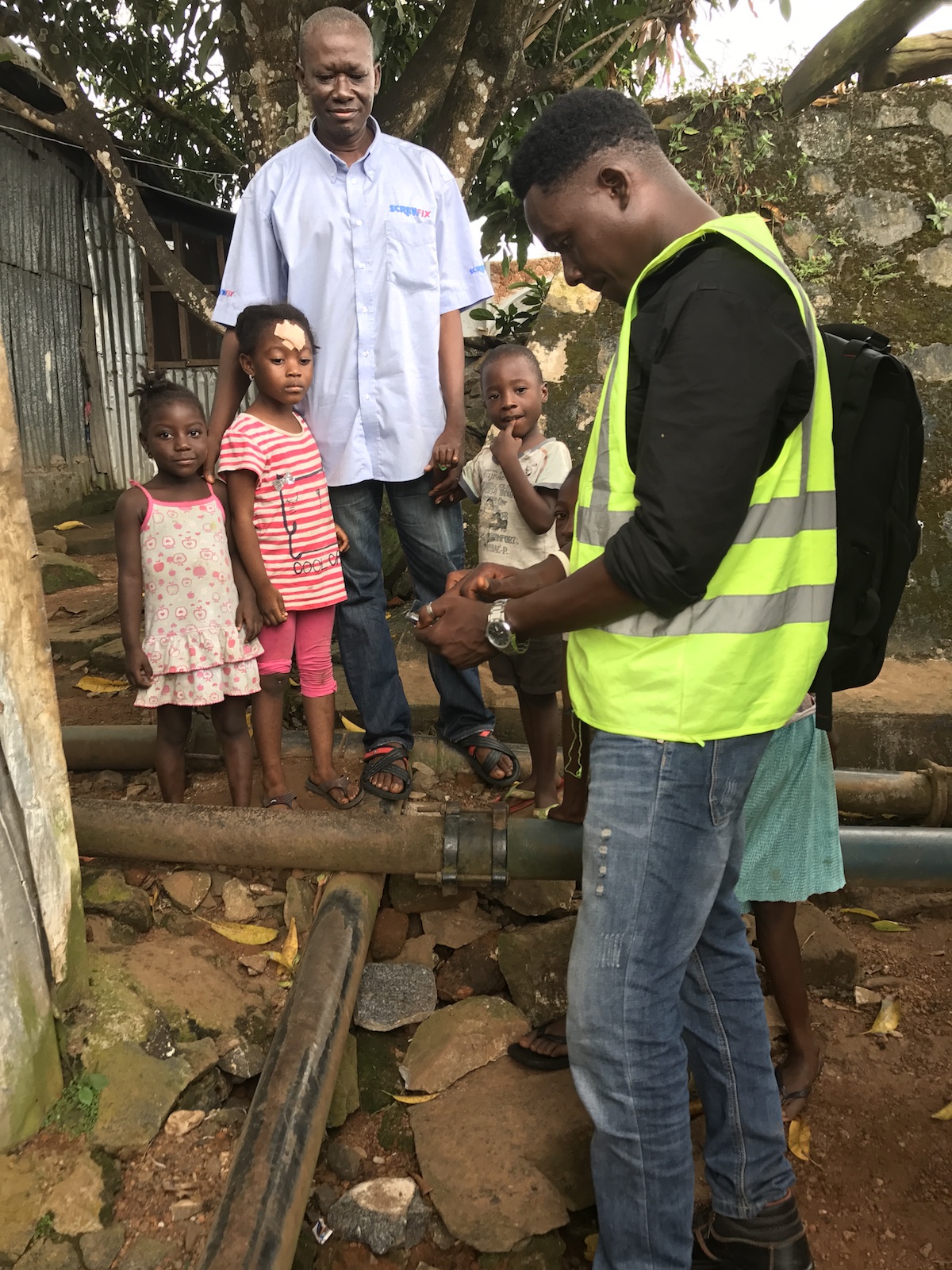 A family looks on as technician Dennis Koroma maps water pipes in Freetown, Sierra Leone.