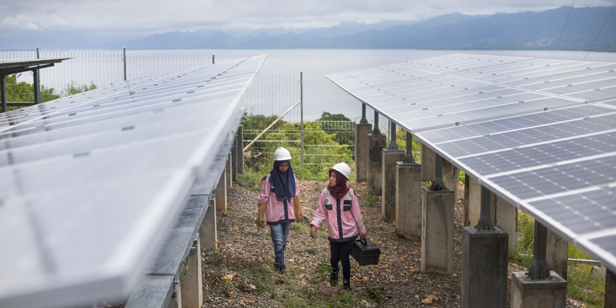 Photo of two women solar technicians in Indonesia walking between rows of solar panels.