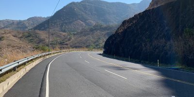 A three lane paved road curving around a mountain
