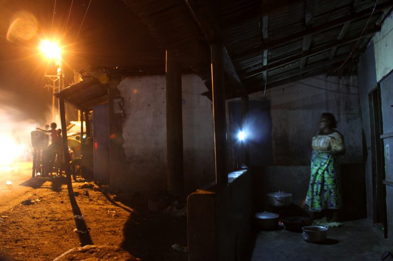 A woman cooking outside in the dark by flashlight in Monrovia, Liberia.
