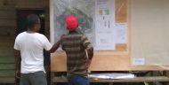 A man with a red hat stands with another man looking at a topographical map