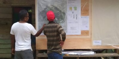 A man with a red hat stands with another man looking at a topographical map