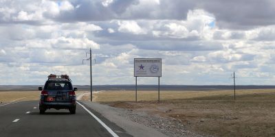 A van drives on a Mongolian road, passing a sign with information about the Mongolia Compact.