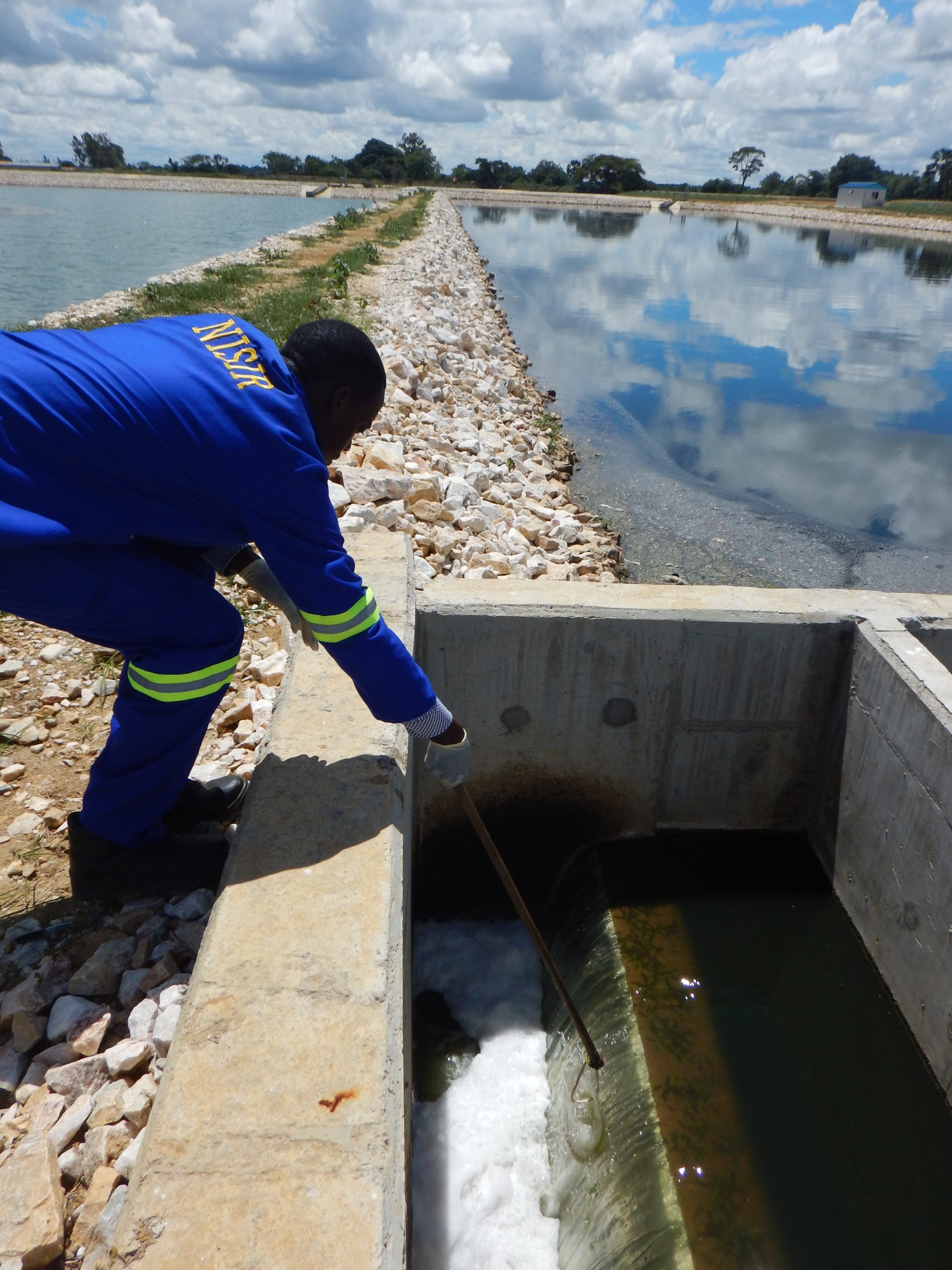 man collecting water samples from waste pond