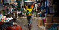 A woman with a baby on her back balances a basin on her head as she walks through a market in Ghana.