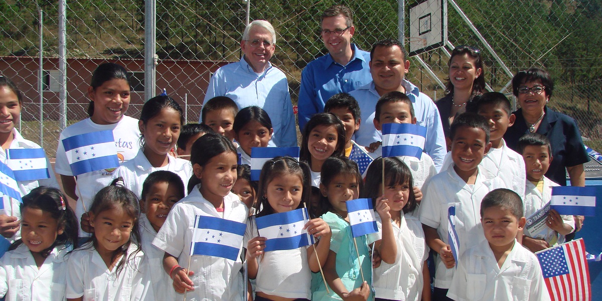 Jonathan Nash (back row, center) celebrates the opening of an MCC-funded school alongside students and Honduran government officials in Colonia Las Pumas in 2011. 